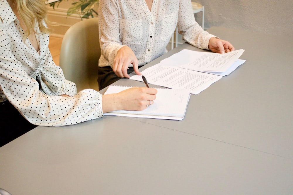 Duas pessoas assinando documentos sobre uma mesa